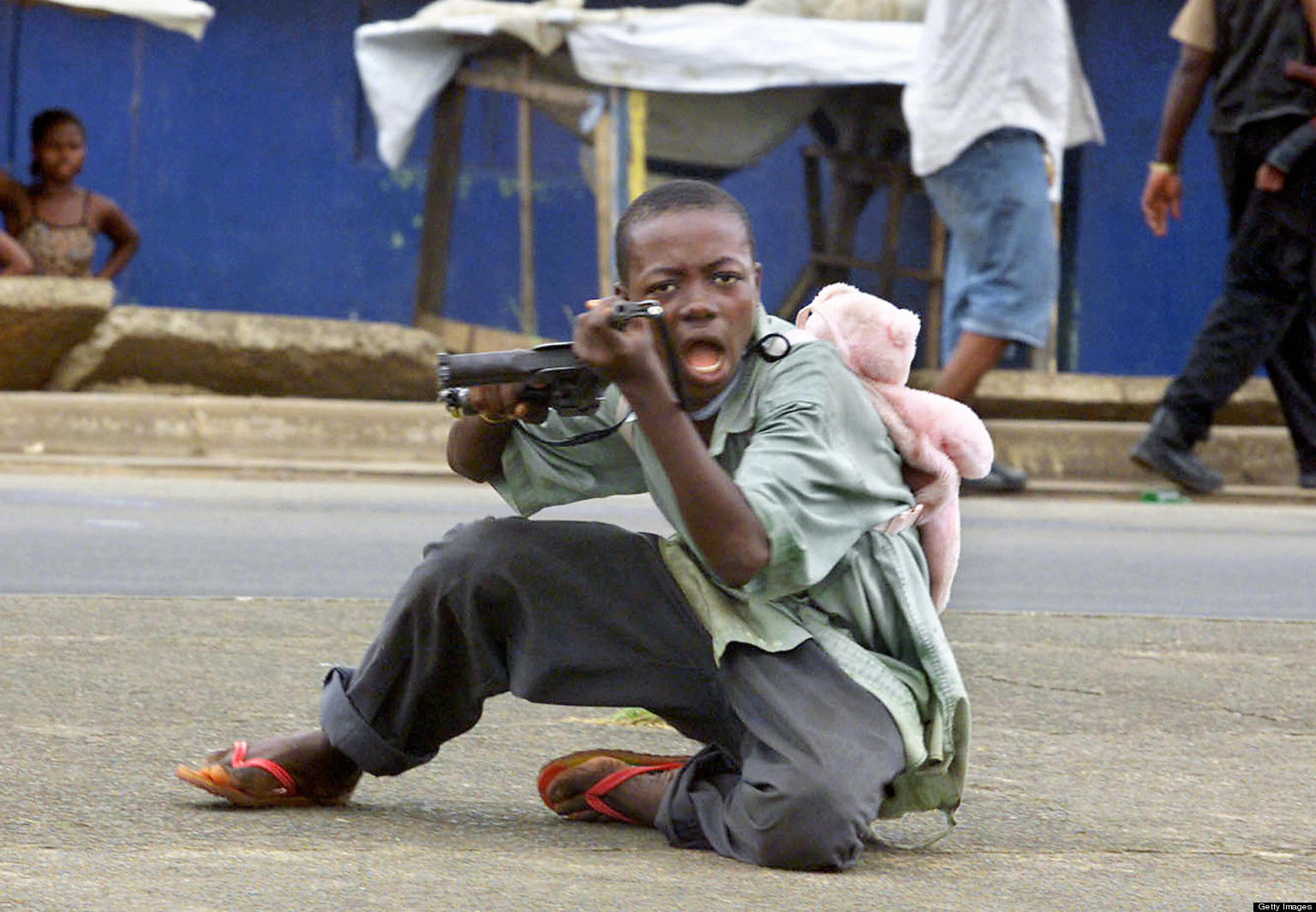 Monrovia, LIBERIA: (FILES) A child soldier wearing a teddy bear backpack points his gun at a photographer in a street of Monrovia 27 June 2003 where Liberian President Charles Taylor's forces took control of the city. At the iniatitve of French Foreign Minister Philippe Douste-Blazy, France will host 05 and 06 February 2007 in Paris an international conference on children involved in armed forces and armed groups called "Let US Free the Children of War". Co-presided by Philippe Douste-Blazy and Ann M. Veneman, executive director of UNICEF, and in the presence of Radhika Coomaraswamy, the UN secretary-general?s special representative for children in armed conflict, the conference will bring together representatives of nearly 60 countries, including many ministers, the European Union, many international organizations, including the United Nations, and representatives of civil society, in particular former child soldiers and NGO leaders active on the ground.  AFP PHOTO FILES GEORGES GOBET (Photo credit should read GEORGES GOBET/AFP/Getty Images)