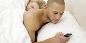 Young man text messaging with young woman sleeping